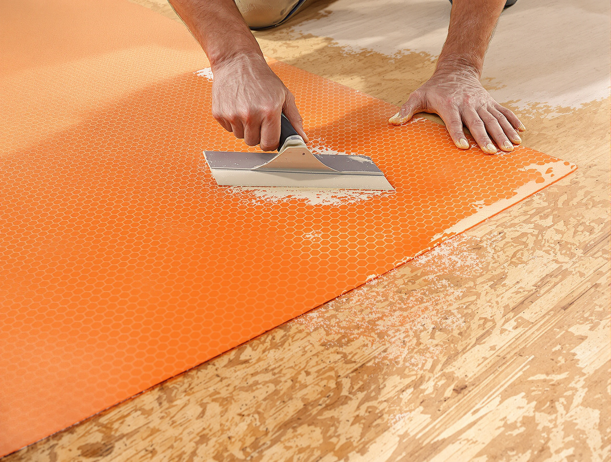 Application soigneuse d'une natte de désolidarisation orange vif sur OSB avec spatule crantée