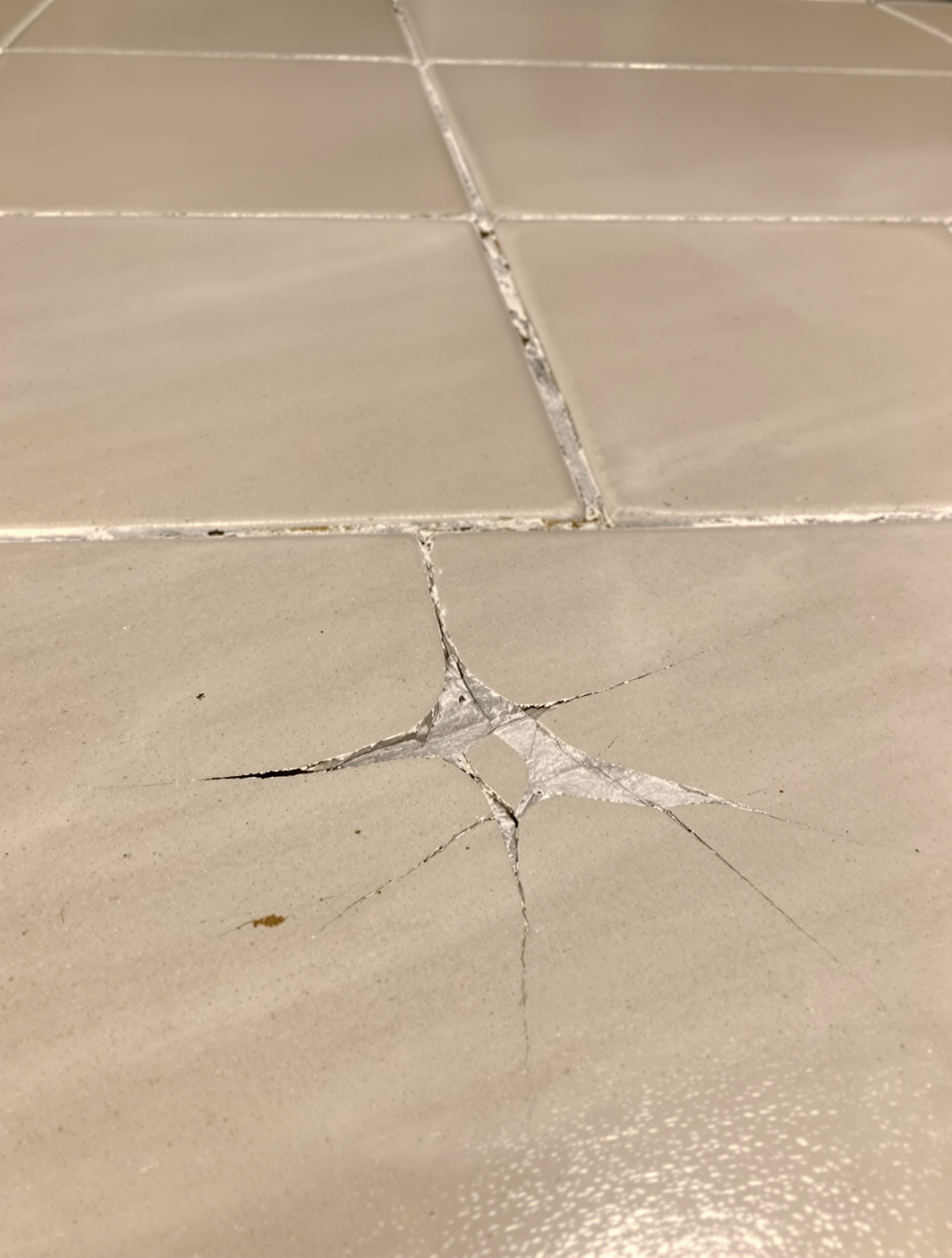 Gros plan sur un carrelage mal posé : joints inégaux, carreaux non alignés, fissure visible – illustration d'un travail bâclé 'au black'.