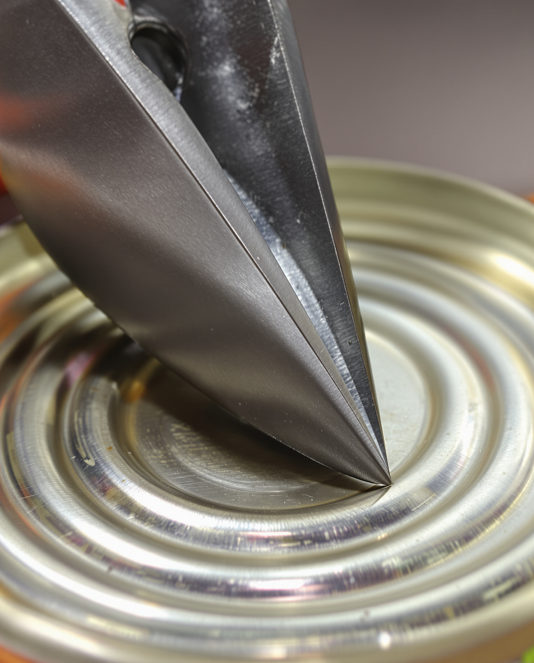 Des ciseaux robustes viennent entamer le couvercle d'une boîte de conserve, la pointe ayant déjà percé un premier trou.