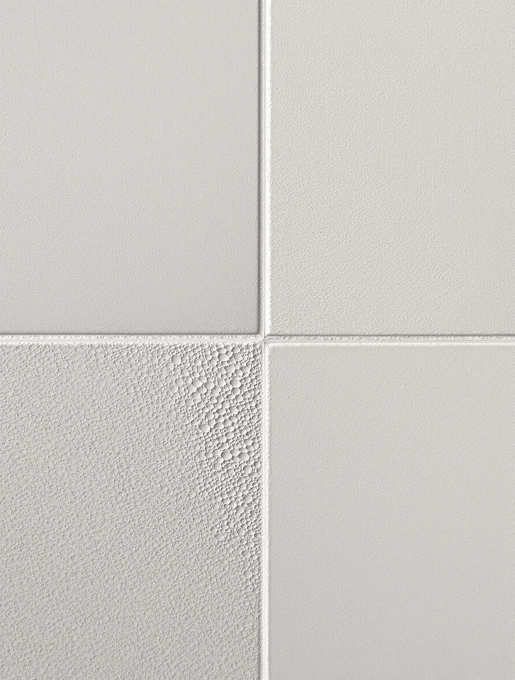 Gros plan sur un joint de carrelage gris clair, parfaitement lissé entre deux grands carreaux effet béton. La lumière rasante met en valeur la texture encore légèrement humide du mortier, suggérant le soin de l'artisan et la phase critique du séchage.