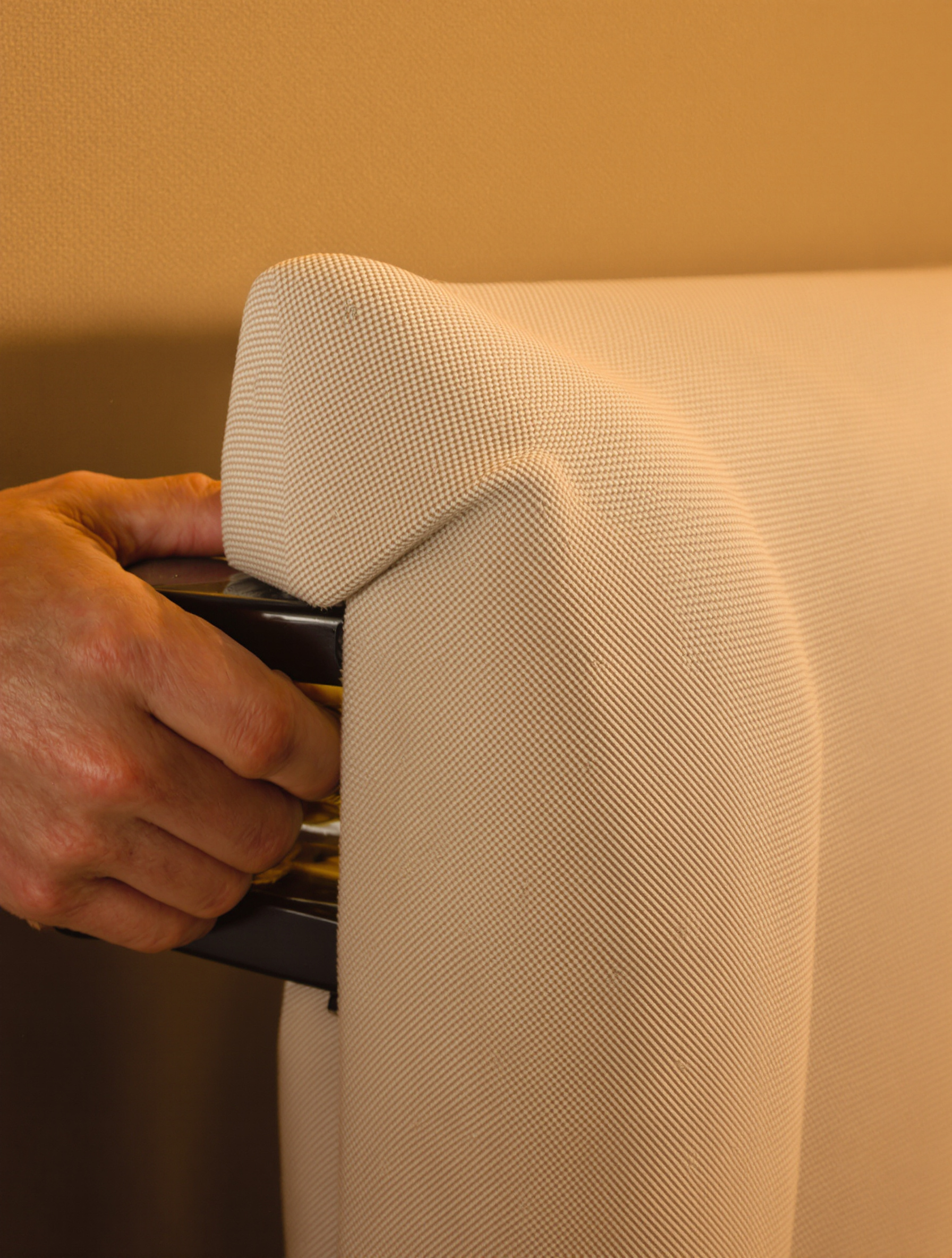 Des mains tendent et agrafent soigneusement un tissu texturé sur une tête de lit.