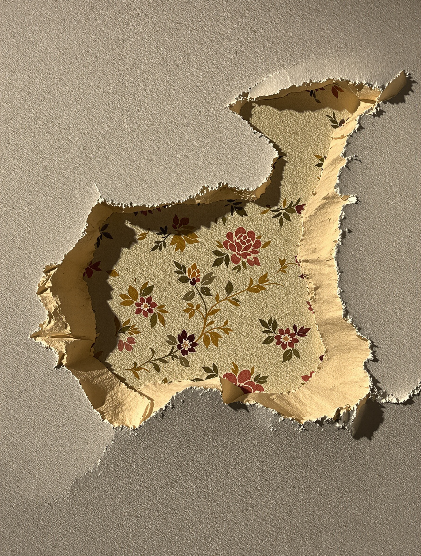 Gros plan sur plusieurs couches de papier peint arrachées : motifs floraux années 70 sous un uni années 90.