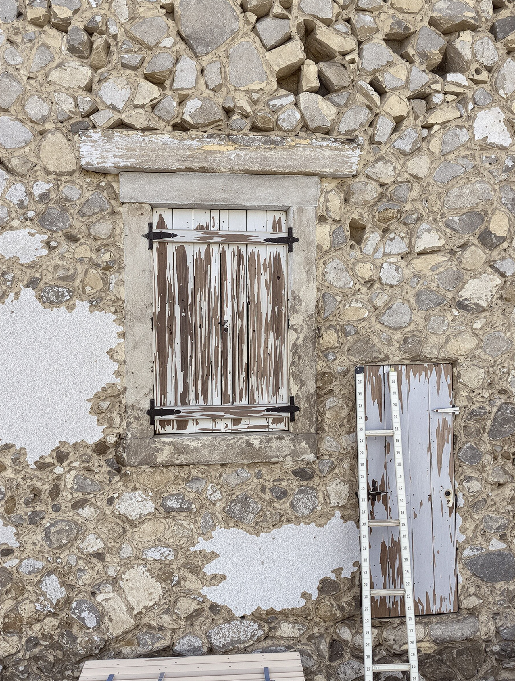 Mur ancien en pierre avec fenêtre en bois et porte, imperfections visibles, mètre ruban posé à côté.