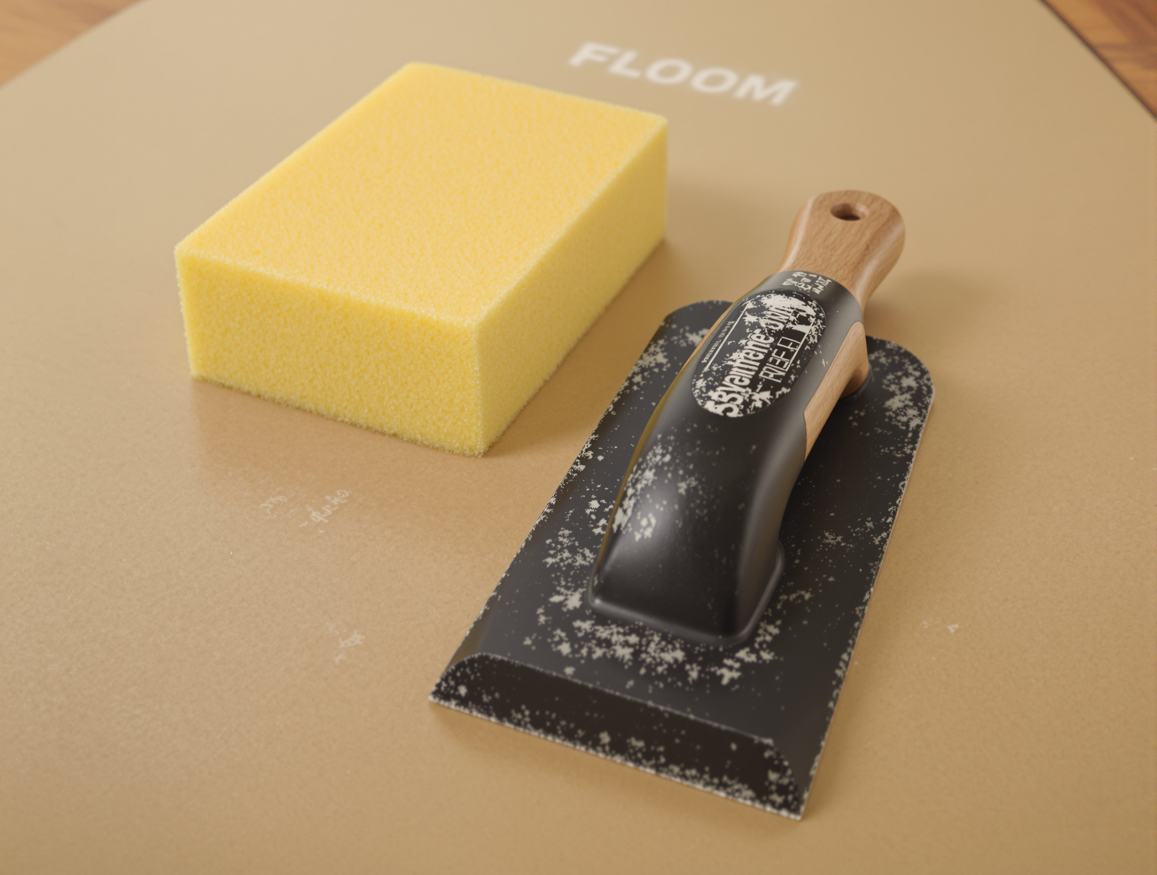 Taloche à jointer en caoutchouc noir et éponge de carreleur jaune sur carton, duo d’outils essentiels pour réaliser des joints de carrelage impeccables.