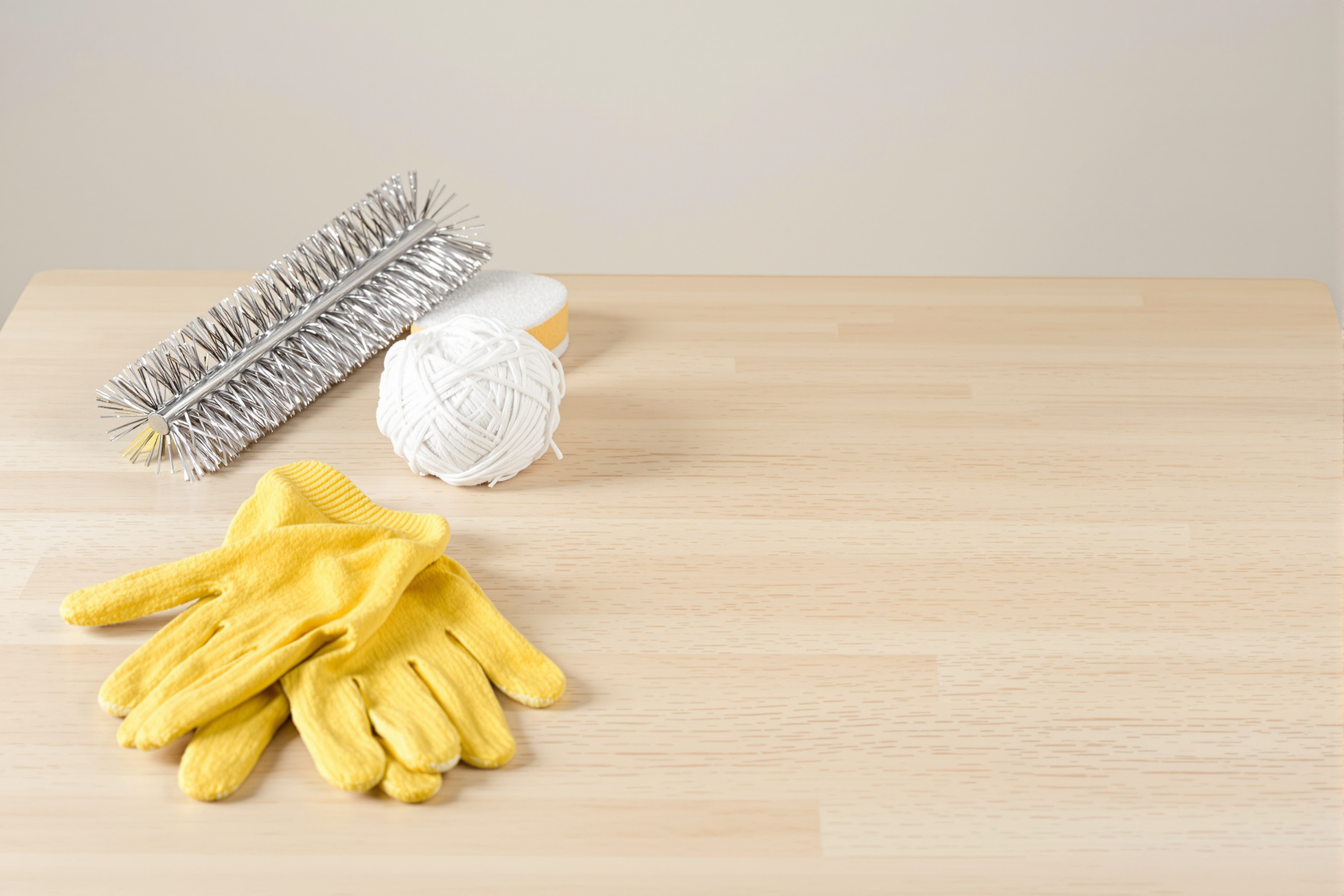 Outils du nettoyage artisanal : brosse métallique, laine d'acier, éponge abrasive et gants sur établi.